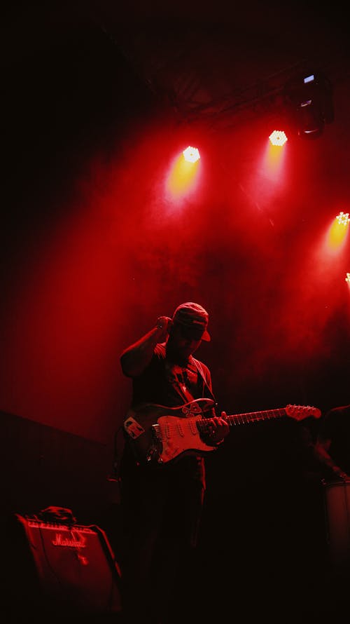 Musician with an Electric Guitar Standing on Stage in Red Lighting 