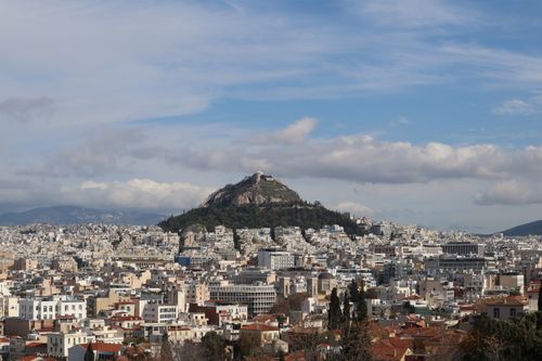 Free Aerial view of Athens, Greece, featuring Mount Lycabettus and city buildings under a partly cloudy sky. Stock Photo
