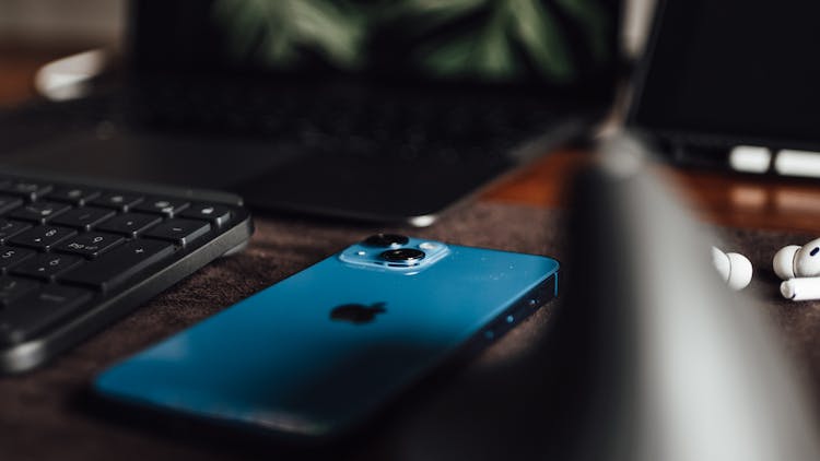 Close-up Of An IPhone, Keyboard, Laptop And Airpods Lying On A Desk 