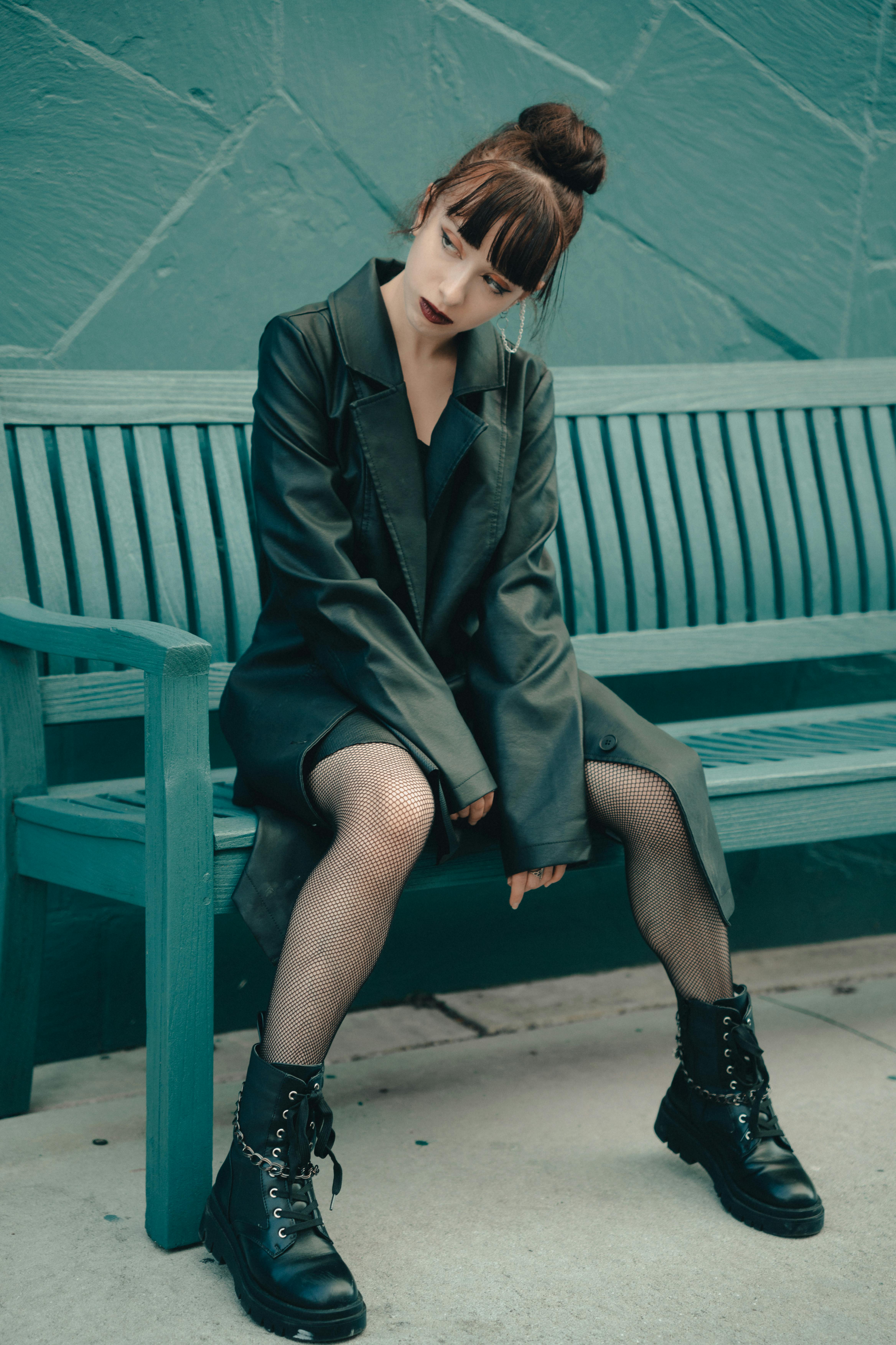 Fashionable woman in a black leather coat and boots sitting on a bench, showcasing urban style.