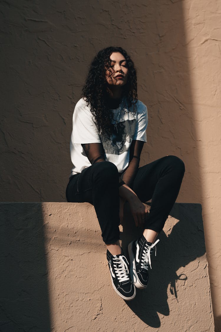 Young Woman In Casual Clothing Sitting On A Wall 