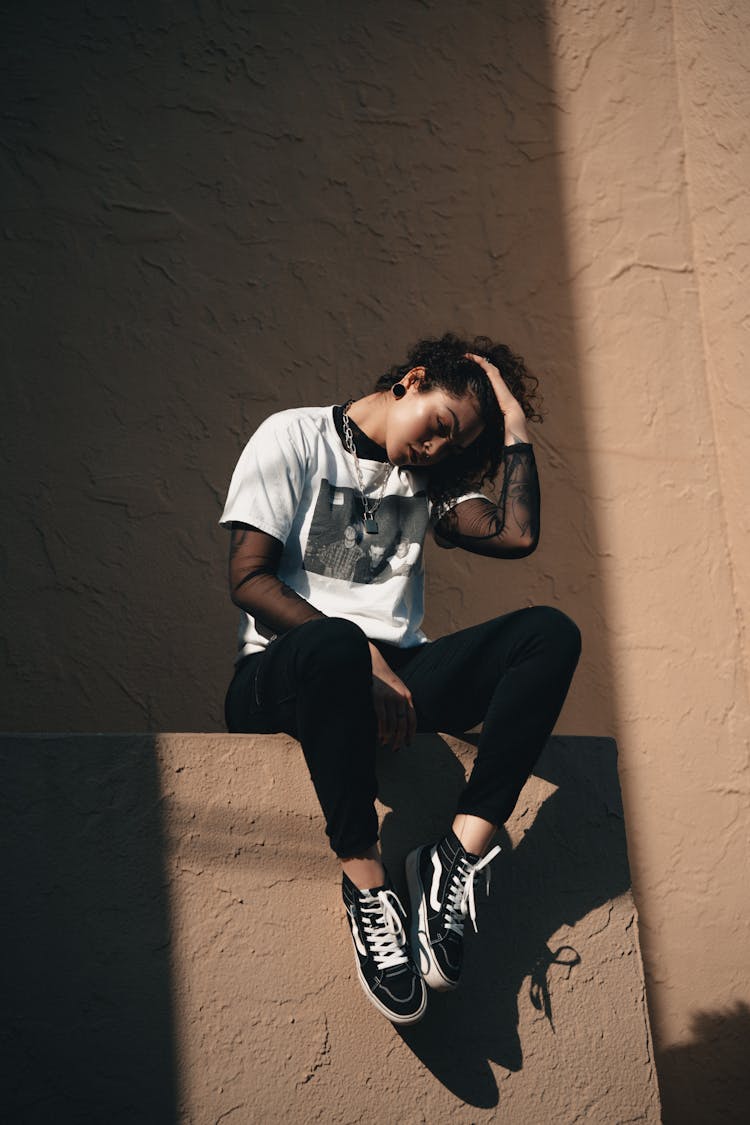 Young Woman In Casual Clothing Sitting On A Wall 