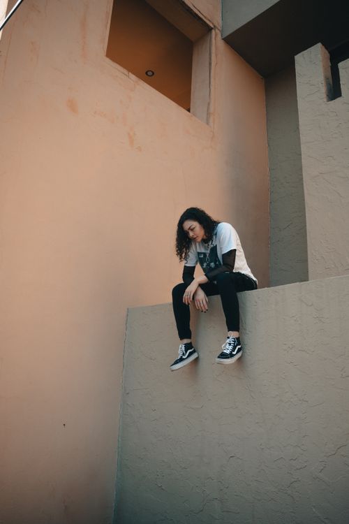 Free Woman in casual clothing sits thoughtfully on an urban wall corner, exuding a sense of contemplation and urban attitude. Stock Photo
