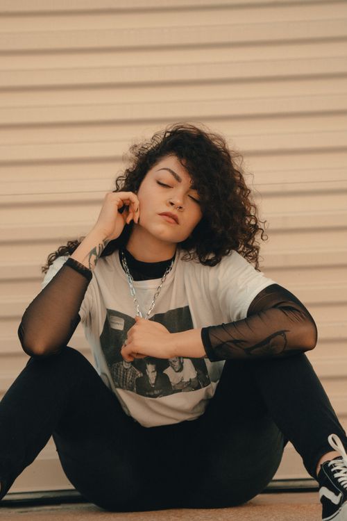 Free Portrait of a stylish woman sitting in urban fashion, with curly hair and a chain necklace. Stock Photo