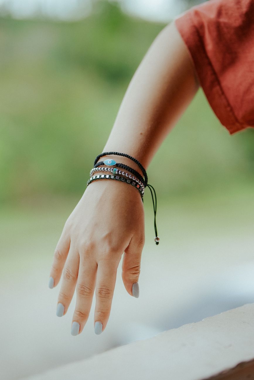 A close-up of a hand adorned with stylish bracelets, set against a blurred outdoor backdrop.