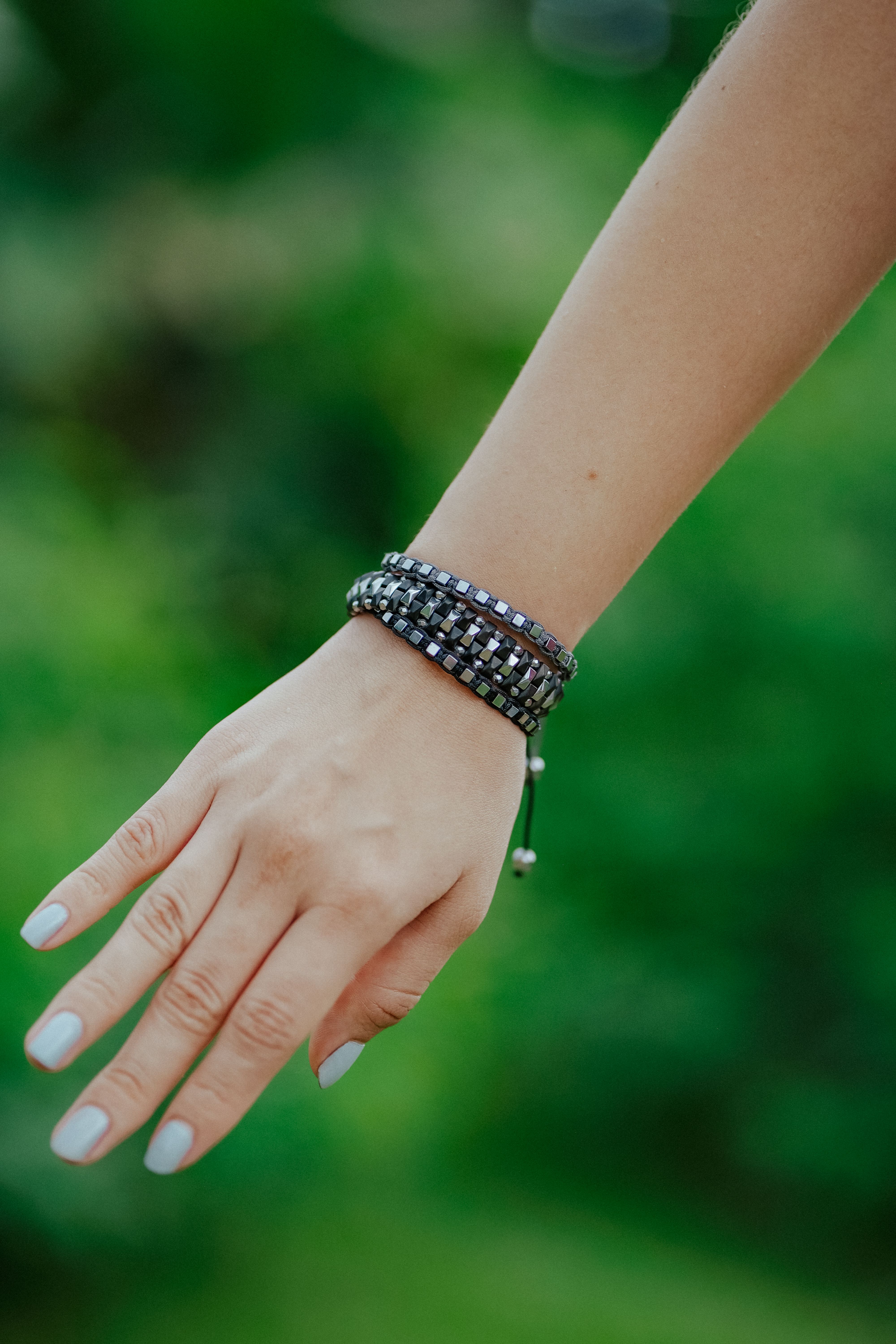 Close-up of a woman's hand wearing a fashionable bracelet against a lush green background.