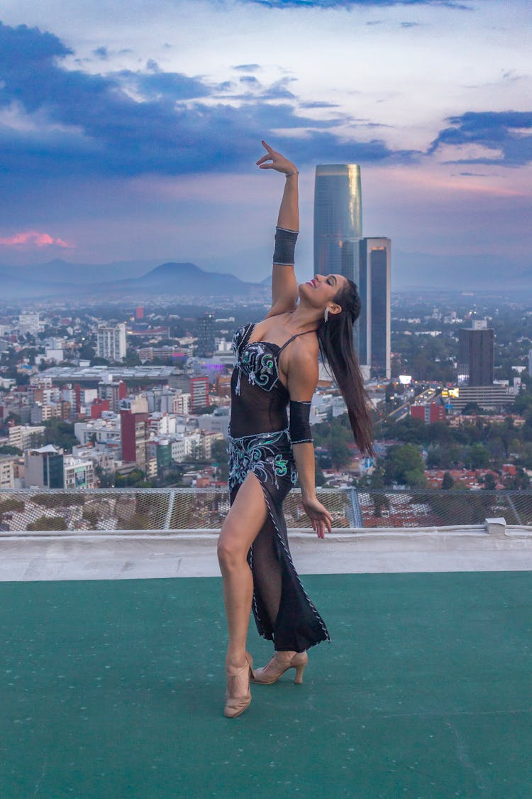 Woman With Long Hair Dancing On A Roof With Cityscape In Background