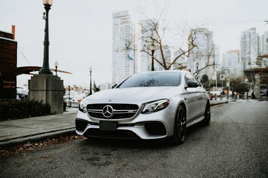 A sleek silver luxury car parked on a city street with skyscrapers in the background.