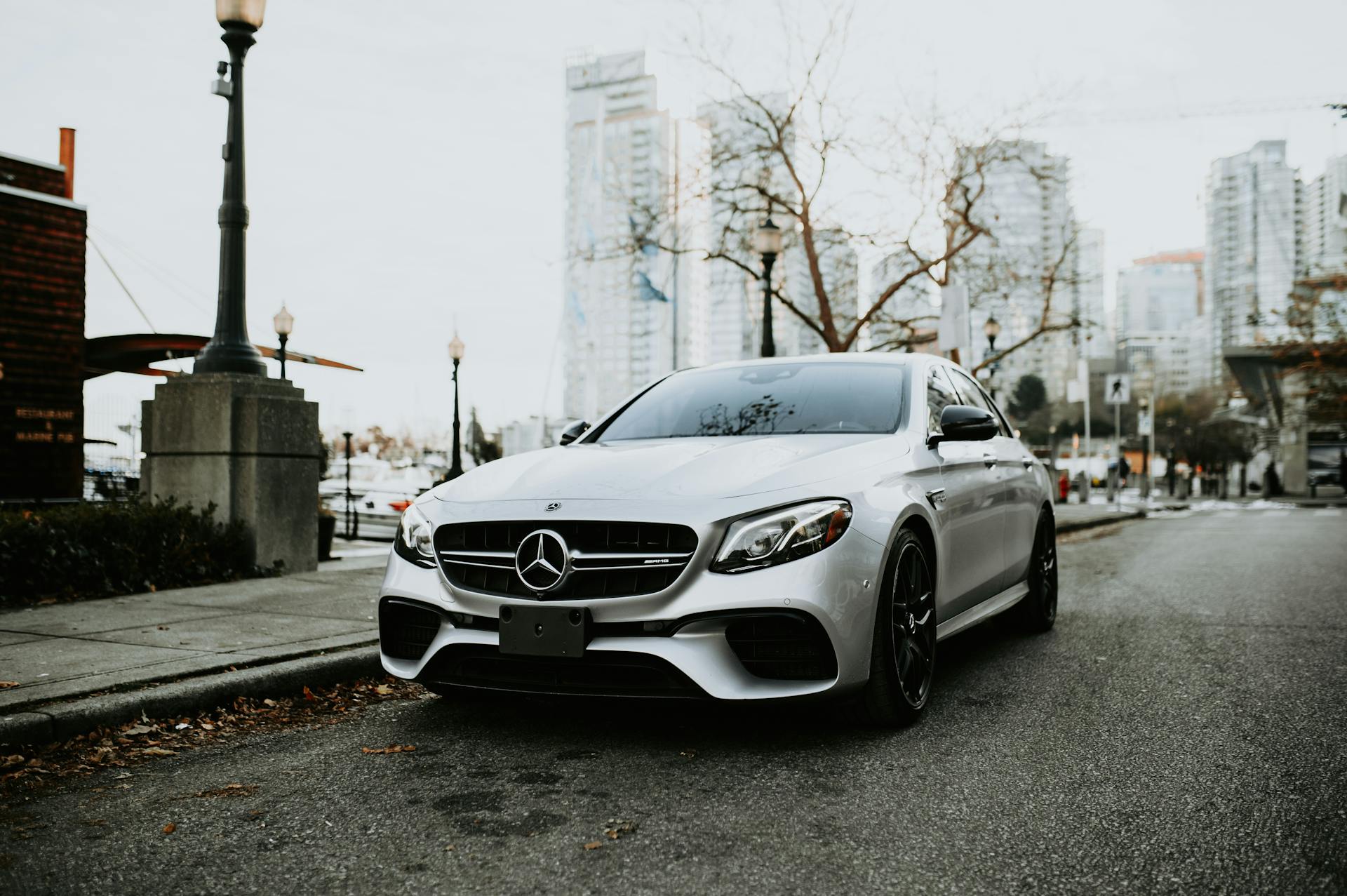 A sleek silver luxury car parked on a city street with skyscrapers in the background.