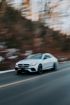 Dynamic shot of a luxury Mercedes car speeding through a forest road, showcasing motion blur.