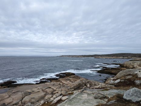 Dramatic seascape of crashing waves on the rocky shore of Peggys Cove, Nova Scotia, on a cloudy day.