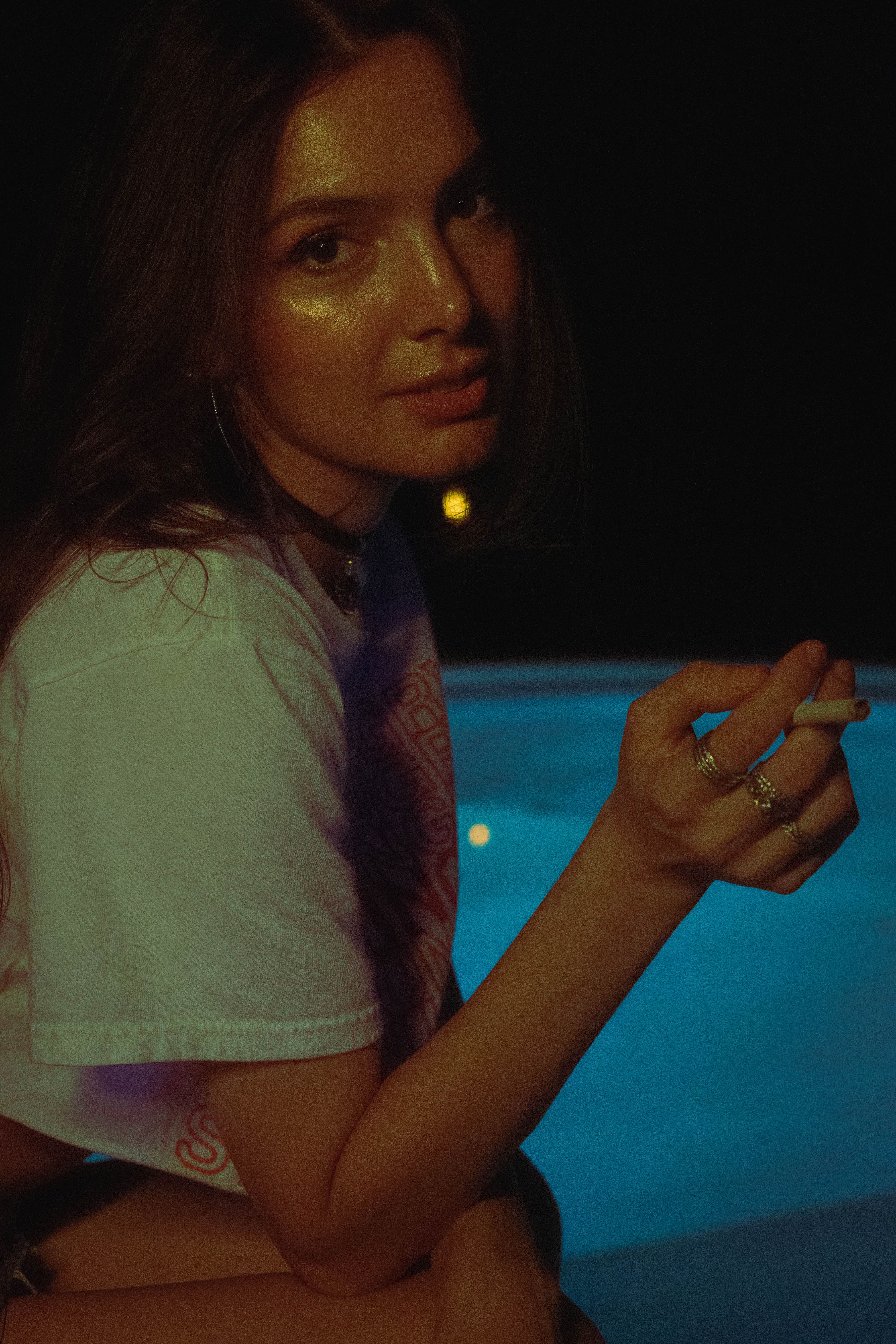 Atmospheric portrait of a woman smoking by a pool at night.