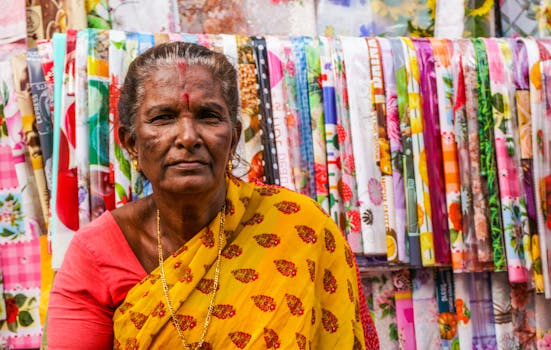 An Indian woman in colorful attire poses at a bustling textile market, showcasing diverse fabrics.