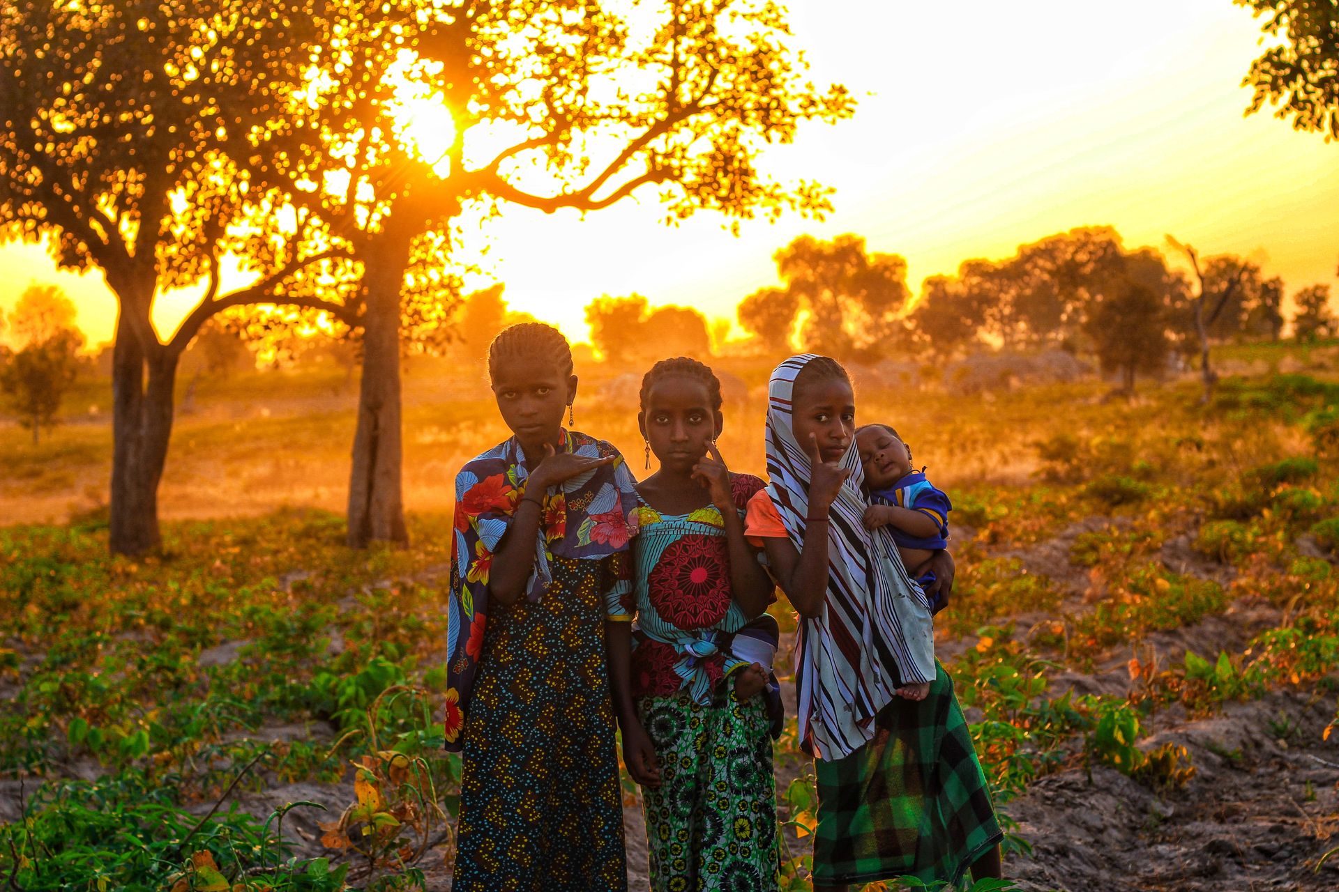 Four African children in a savannah landscape at sunset, showcasing vibrant colors and cultural attire.