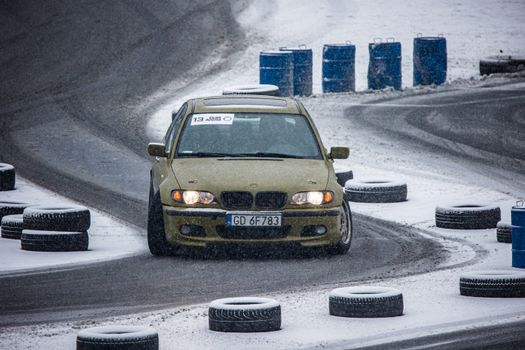 A BMW car expertly drifts on a snow-covered track, showcasing winter motorsport skills.