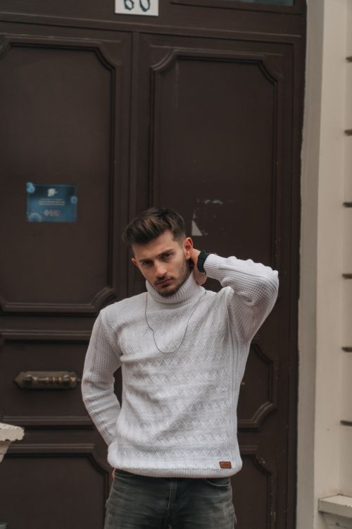 Free A fashionable man posing in a white turtleneck sweater against a rustic door in Istanbul. Stock Photo