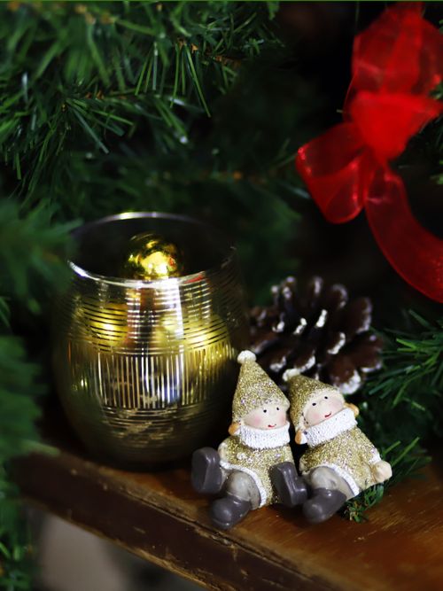 Free Adorable Christmas figurines beside a candle and pine cone on a decorated tree. Stock Photo