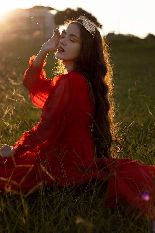 Portrait of Beautiful Woman in Red Dress Sitting in Field