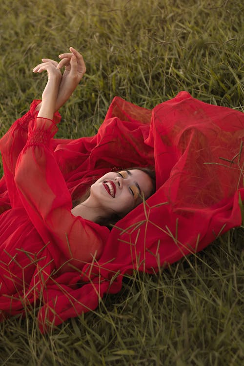 Portrait of Beautiful Woman in Red Dress Lying in Field with Hands in the Air