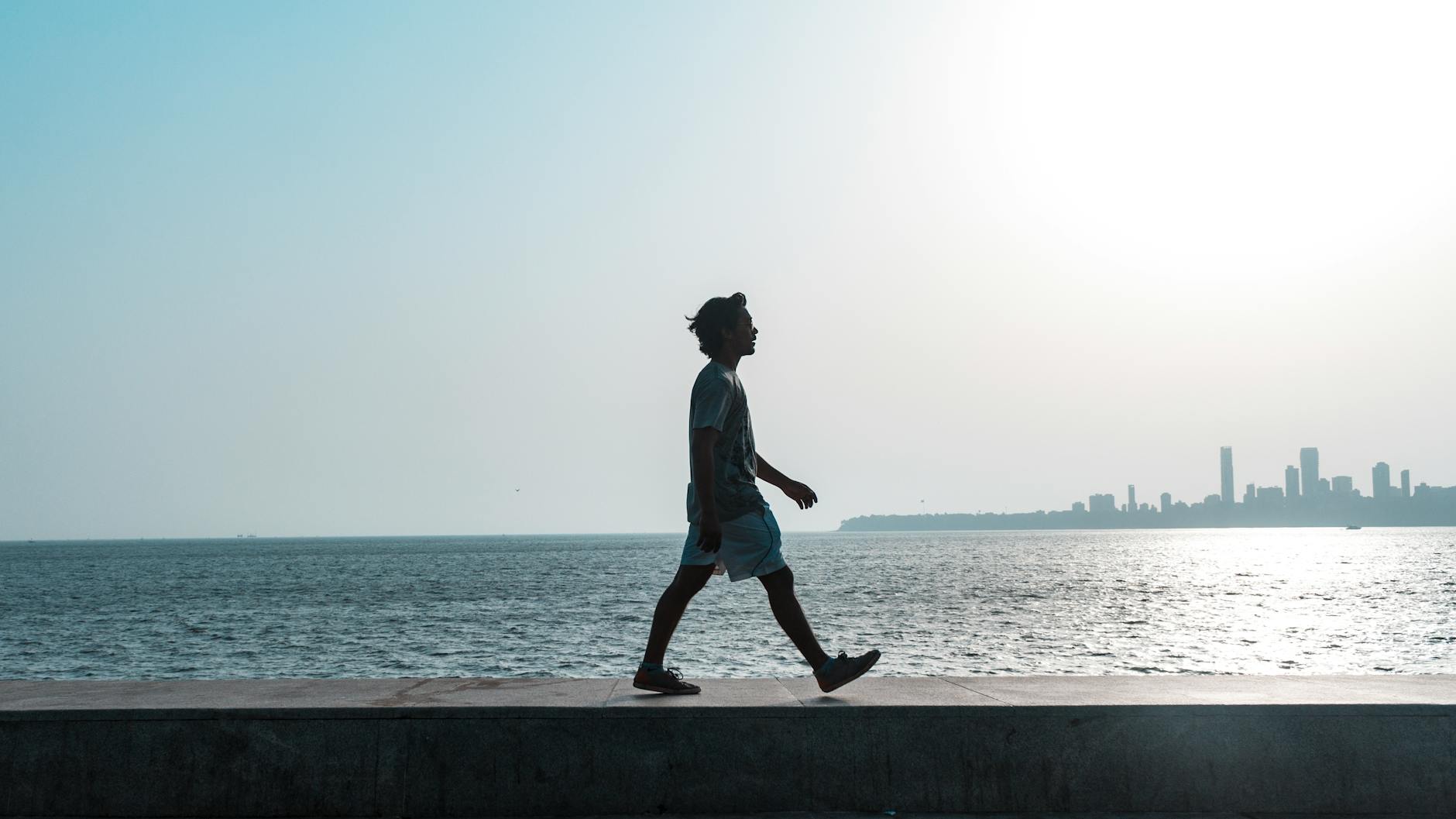 A silhouette of a man walking along the Mumbai coastline at sunset with a cityscape backdrop.