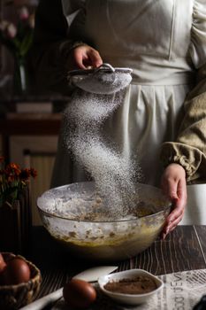A woman sifting powdered sugar into a mixing bowl, creating a classic baking scene.