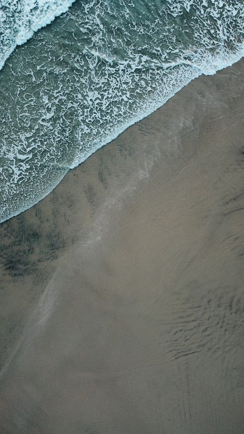 Free Drone shot capturing waves crashing on a sandy shore, providing a calming beach scene. Stock Photo