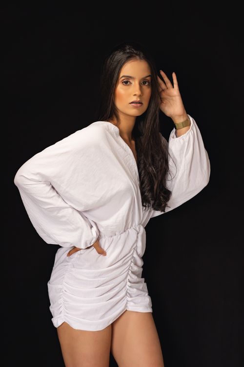 Free Portrait of an elegant young woman posing in a white dress against a black background. Stock Photo