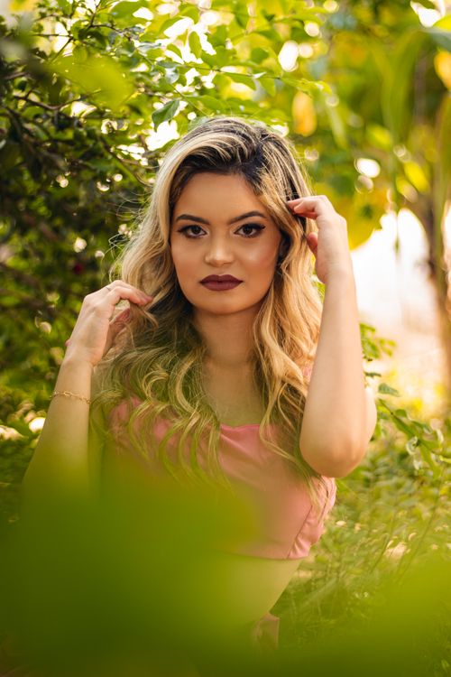 Free Elegant blonde woman with makeup posing amidst lush green foliage outdoors. Stock Photo
