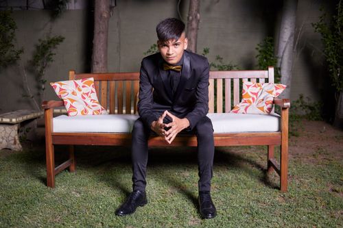 Free Young man in a black suit sitting confidently on a wooden bench outdoors. Stock Photo