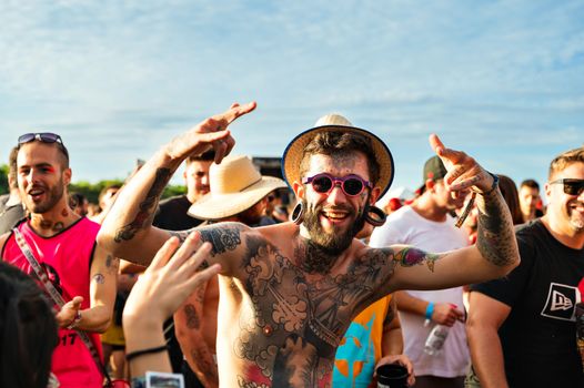 Young adults enjoying a lively summer music festival with colorful tattoos and stylish sunglasses.