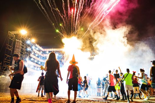 A lively crowd enjoys a nighttime festival with dazzling fireworks and vibrant lighting.
