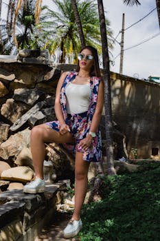 一位戴着太阳镜的时尚女性，身着花卉服装，自信地在户外岩石与绿植间摆着姿势