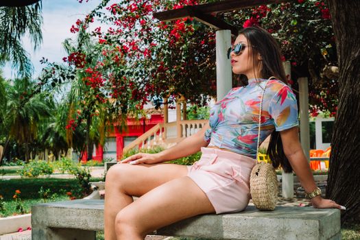 夏天，一位戴着墨镜的时尚女性坐在花园的长凳上，花园里充满活力