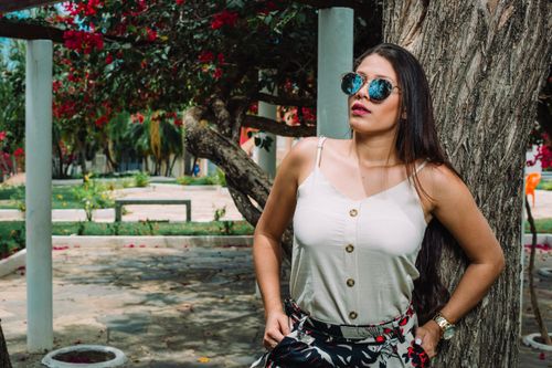 Free Fashionable woman in sunglasses leans against a tree outdoors, exuding confidence and style. Stock Photo