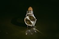 经典的银色手表搭配皮革表带，在反光表面上展示，尽显淡雅气质