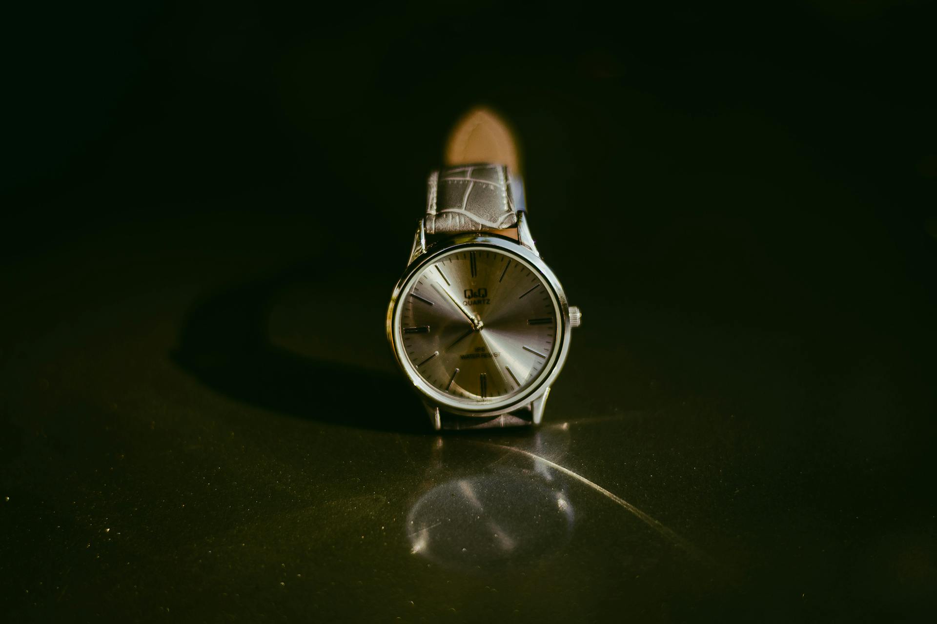 Classic silver wristwatch with leather strap showcased on a reflective surface, perfect for a touch of elegance.