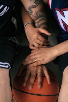 Close-up image of hands with tattoos resting on a basketball, symbolizing teamwork and connection.