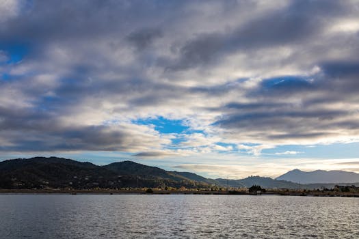 Breathtaking view of mountains beneath dramatic clouds over a serene water body during the day.