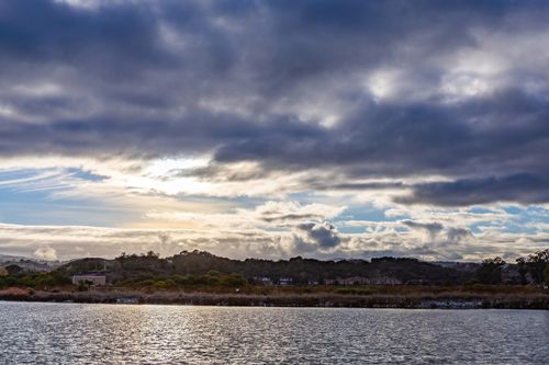Free Captivating view of a river under a dramatic cloudy sky with sunlight breaking through, creating a moody atmosphere. Stock Photo