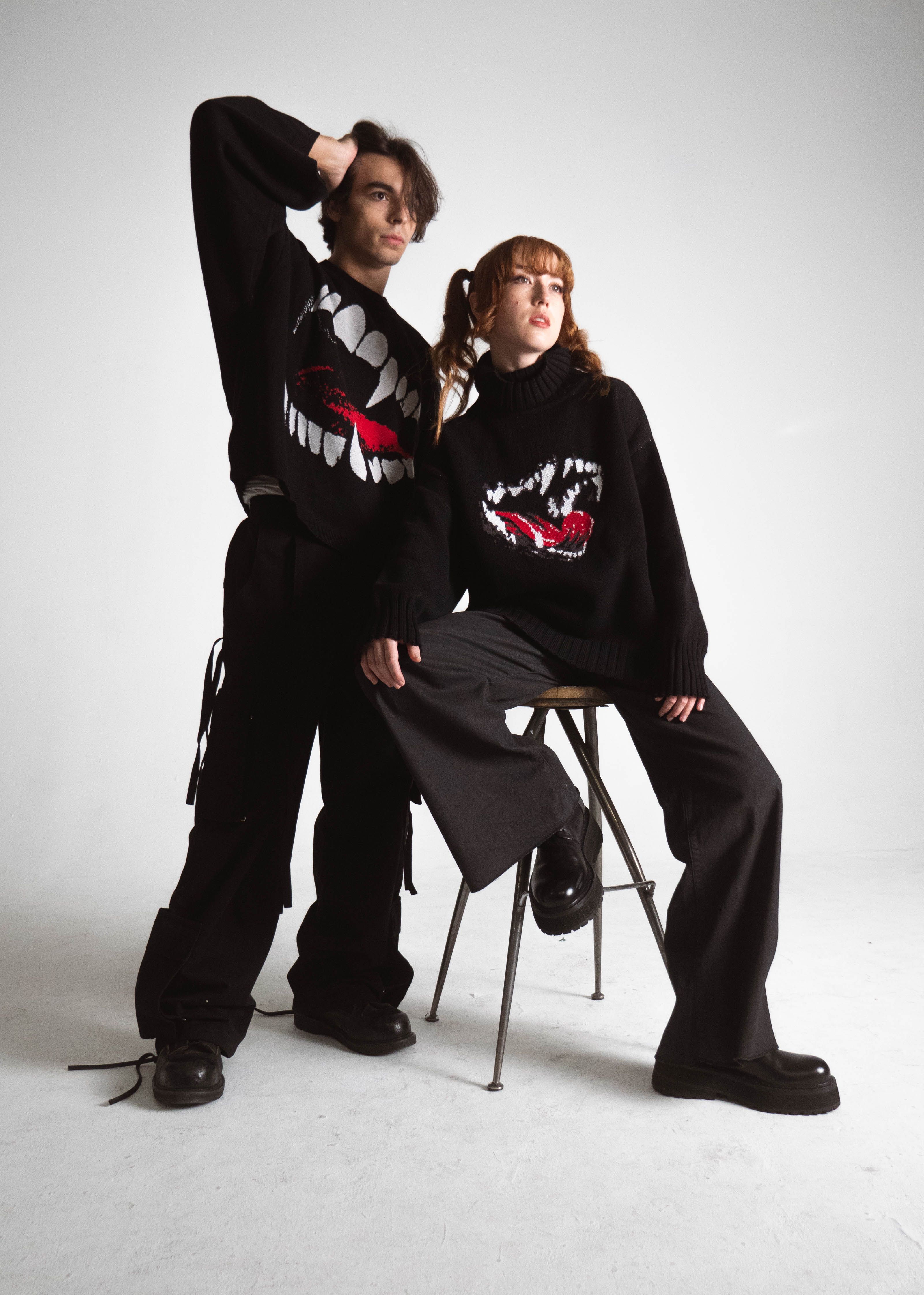 Fashion photo of two young models in vampire-themed sweaters, posing in a studio.