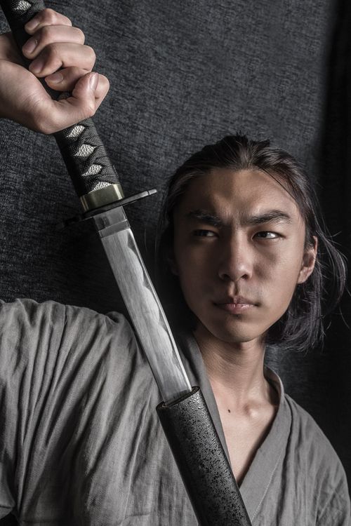 Free East Asian man portrays a samurai, holding a katana, exuding intensity and focus. Stock Photo