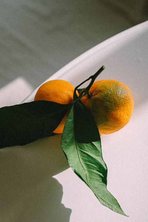 Free Close-up of fresh oranges with green leaves on a sunlit table, highlighting natural textures. Stock Photo