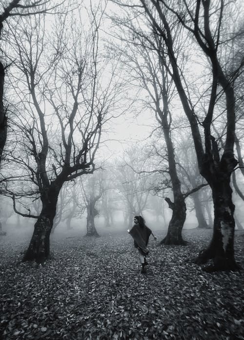Grayscale Photo of Woman Running Beside Leafless Trees