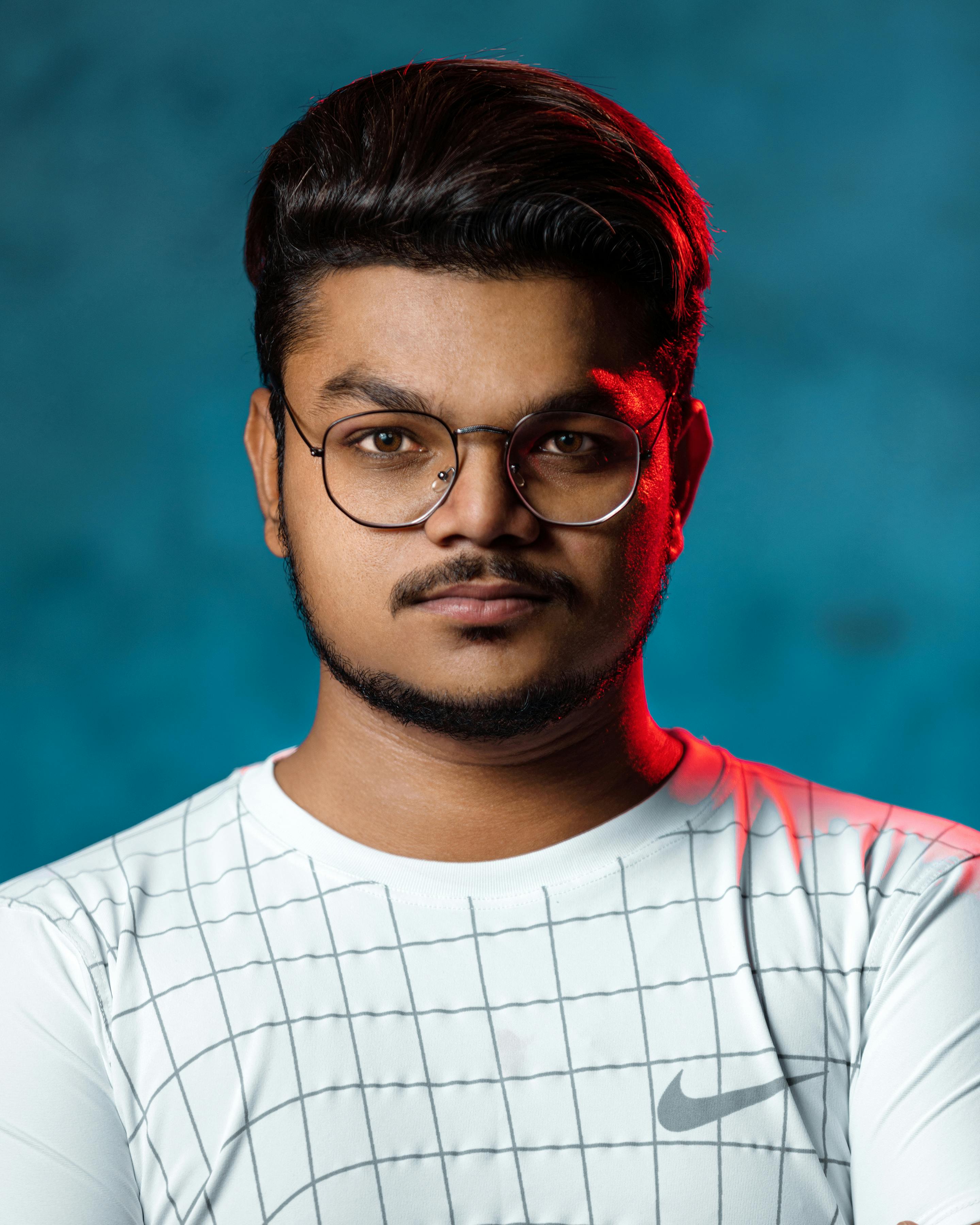 Studio portrait of a confident young man in eyeglasses and casual attire against a blue background.