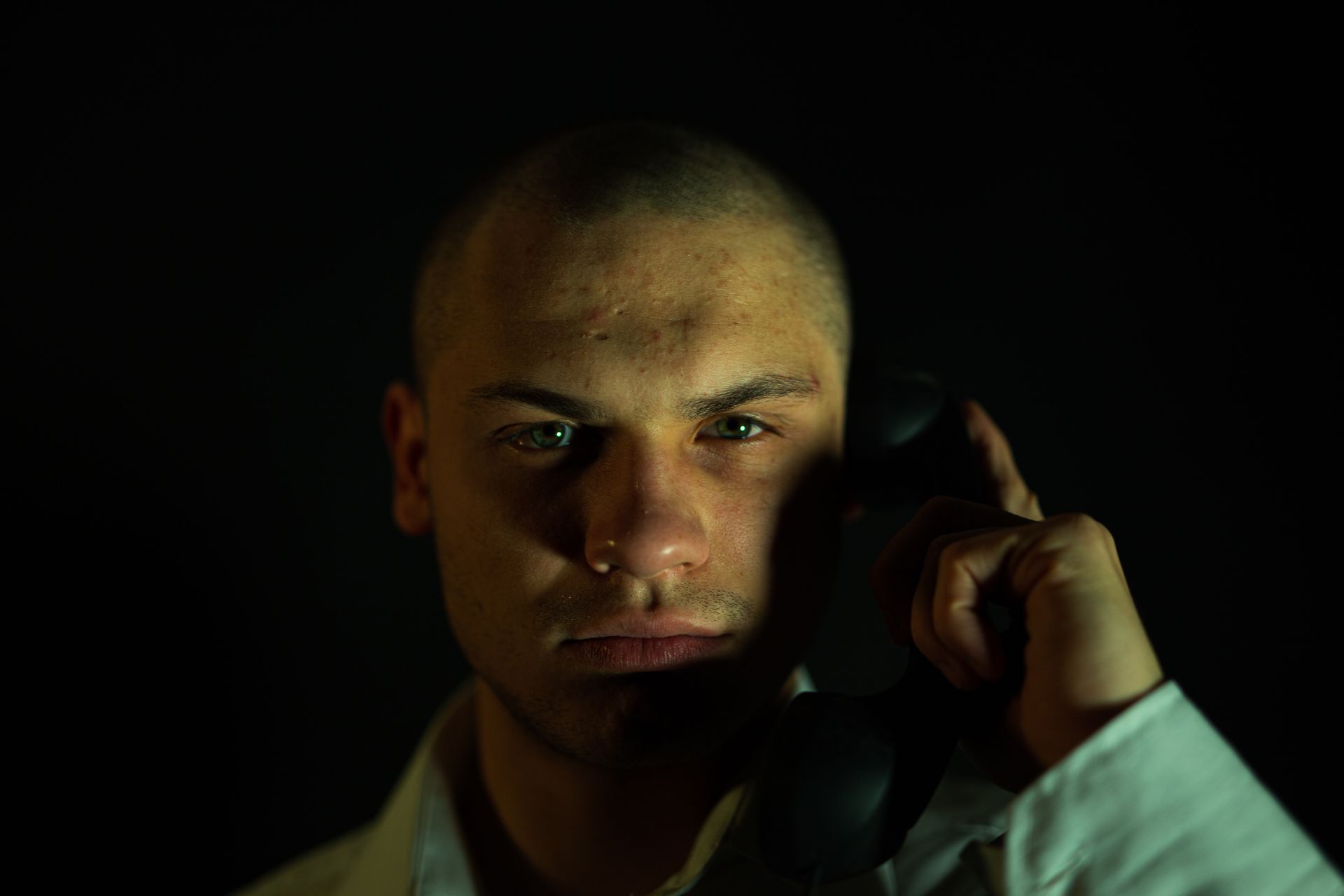 A dramatic portrait of a person holding a vintage phone against a dark background.