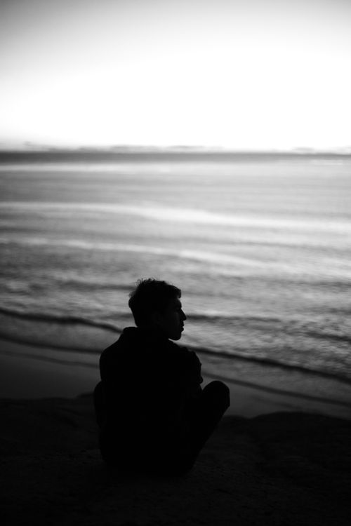 Free A contemplative silhouette of a man sitting by the tranquil sea during twilight in black and white. Stock Photo