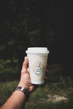 特写：手持纸咖啡杯在自然的户外环境中