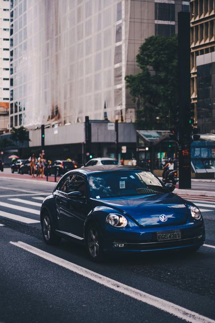 Blue Volkswagen Beetle driving on Paulista Avenue, São Paulo's urban scene.