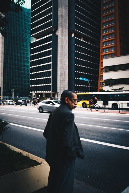 Candid urban street scene in Bela Vista, São Paulo, featuring a man walking past city skyscrapers.