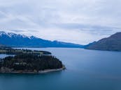 从鸟瞰图中可以看到，一个宁静的湖泊被郁郁葱葱的绿色植物和新西兰白雪皑皑的山脉环绕，景色令人惊叹